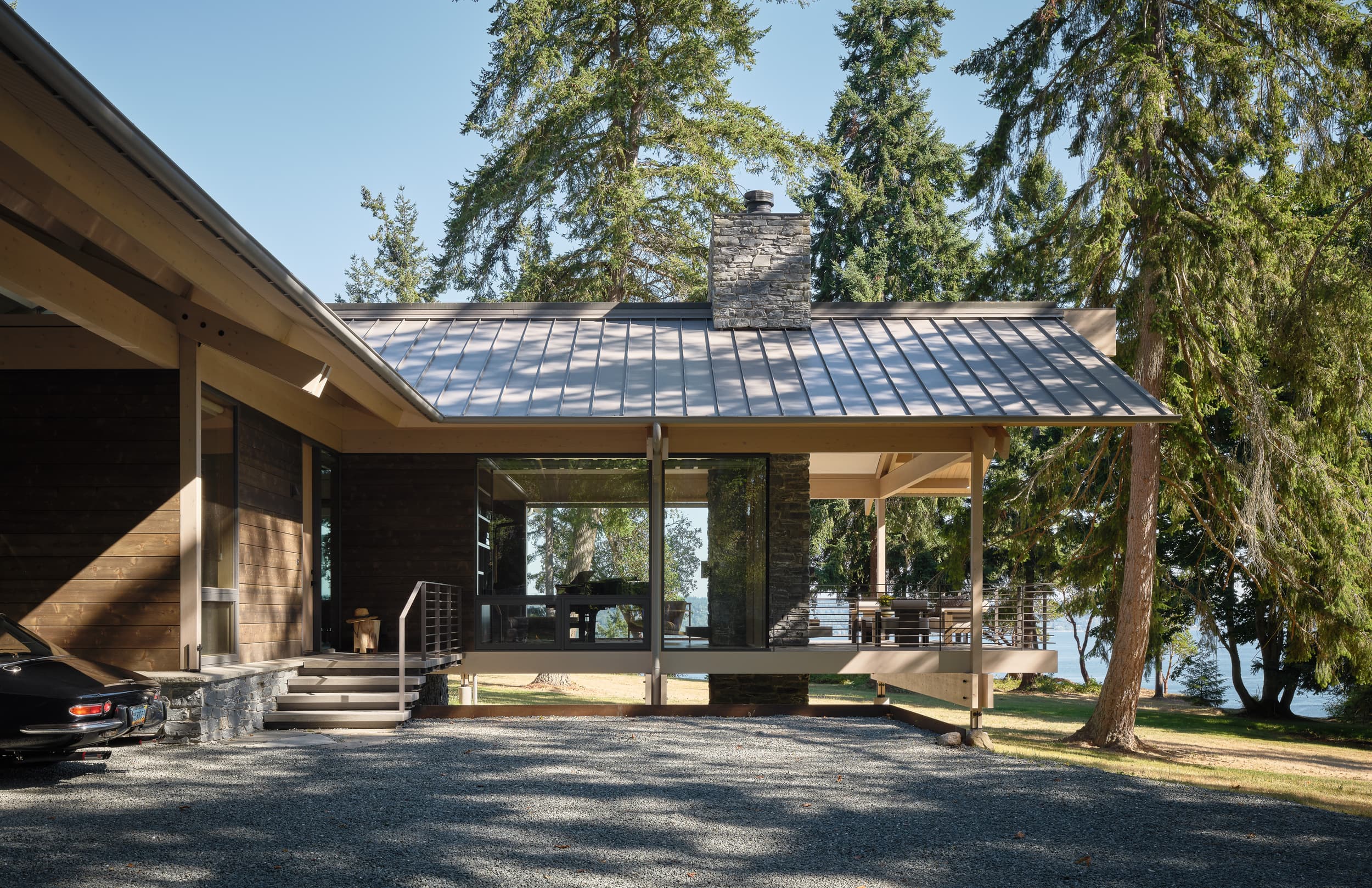 A tan, mid-century modern house with a tiled roof, set in a forest by the water.