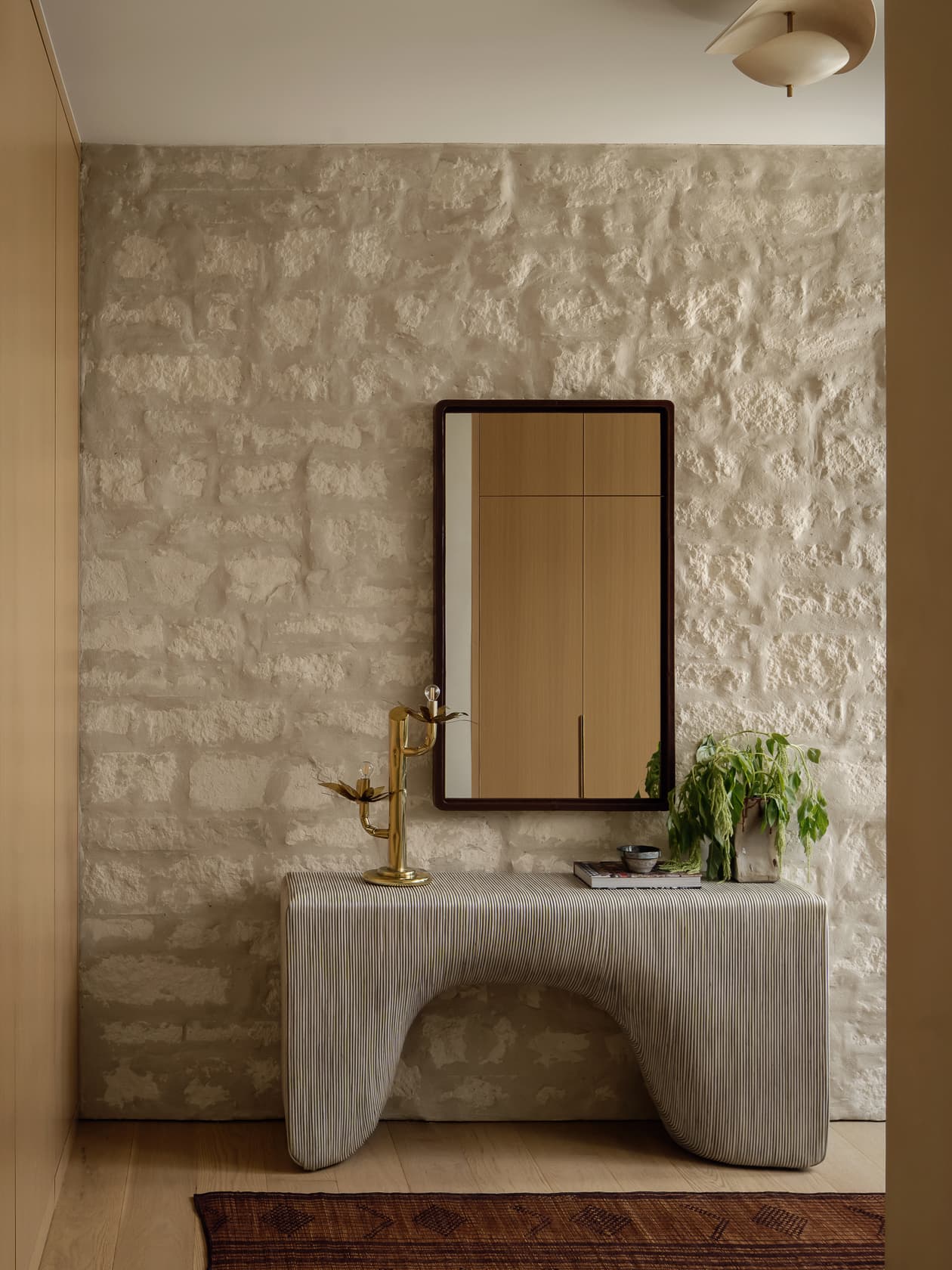 A modern sculptural console table against a rustic, light-colored stone wall in a hallway.