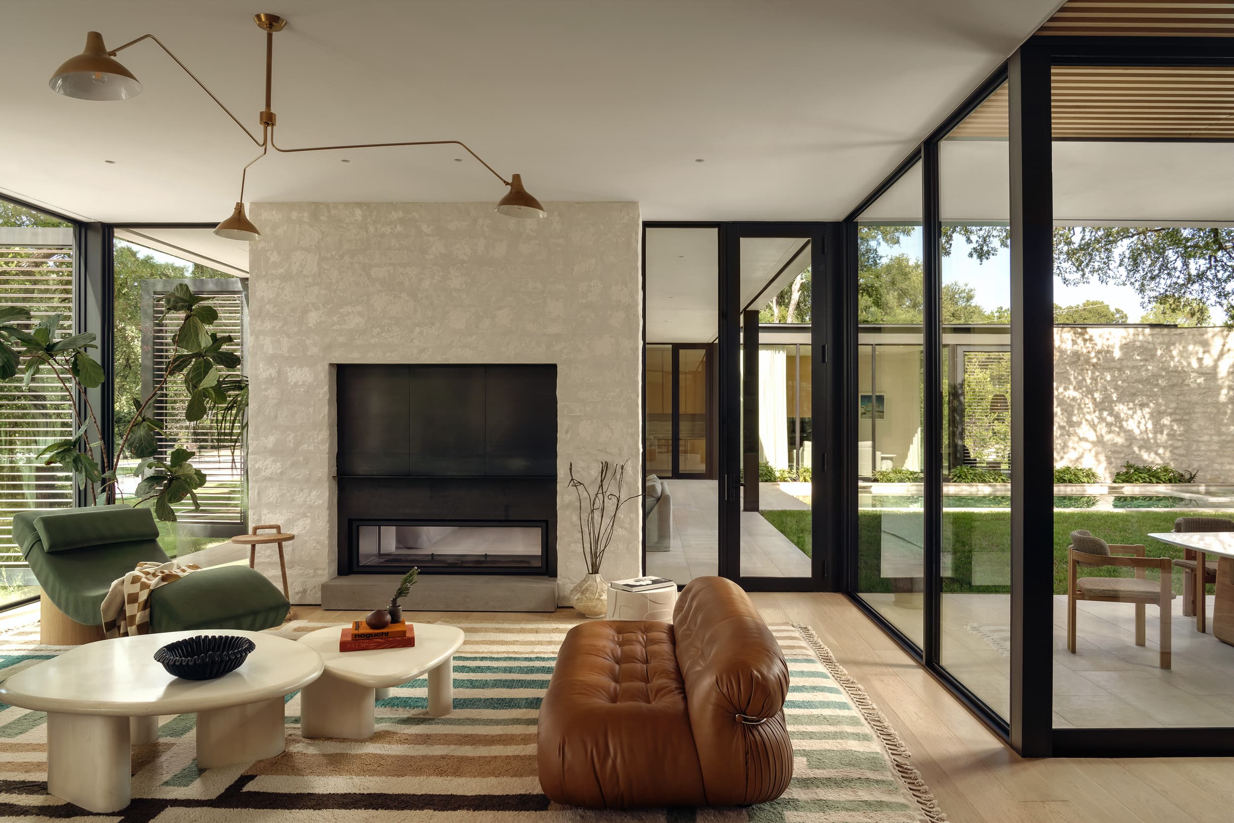 A bright living room with a brown leather sofa, a stone fireplace, and floor-to-ceiling windows.