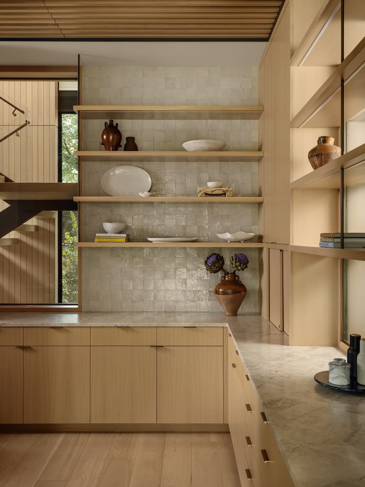 Modern kitchen with light wood cabinets, open shelving, and a textured tile wall.