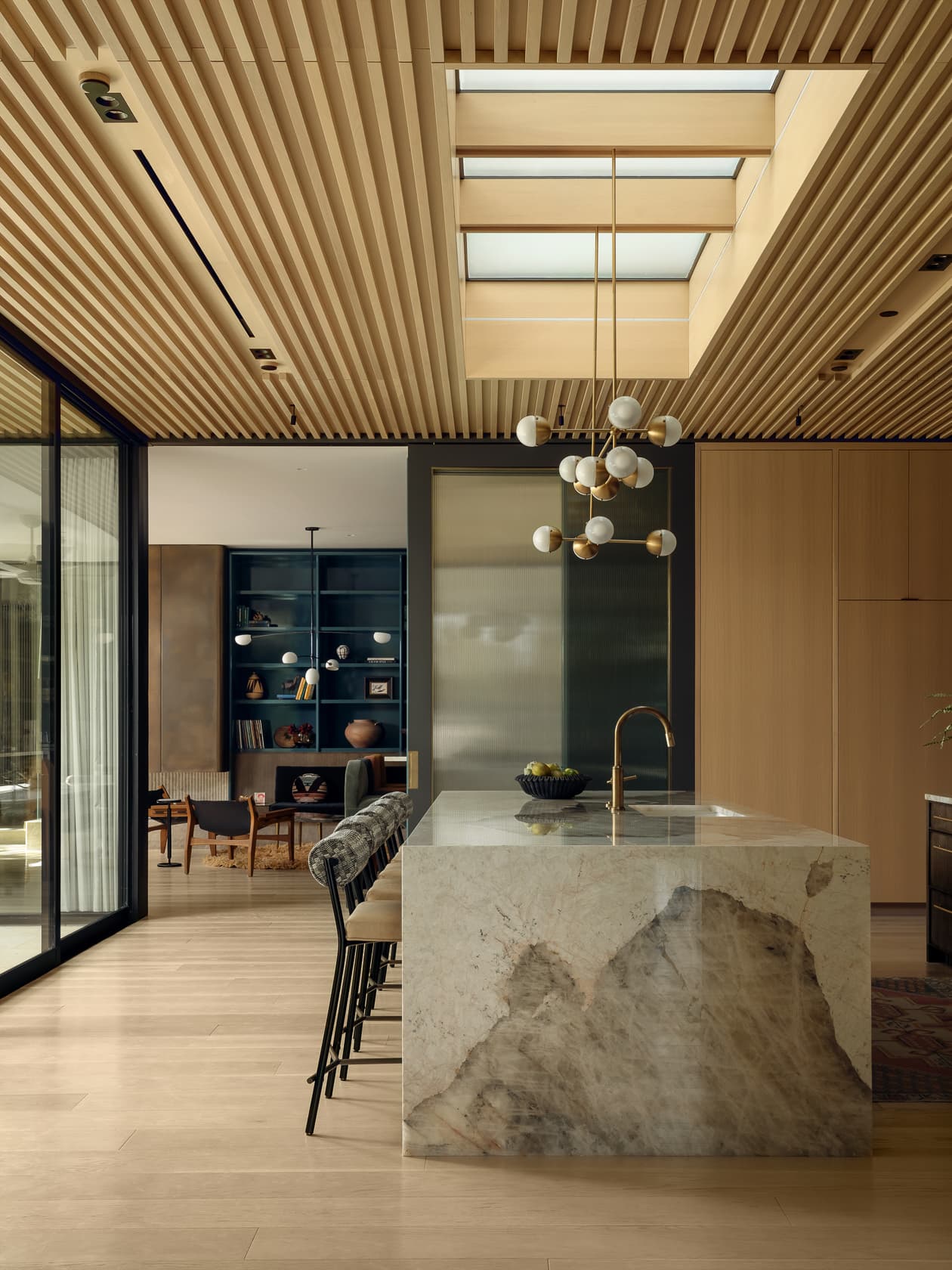 A modern kitchen with a dramatic stone island under a slatted wood ceiling and skylight.