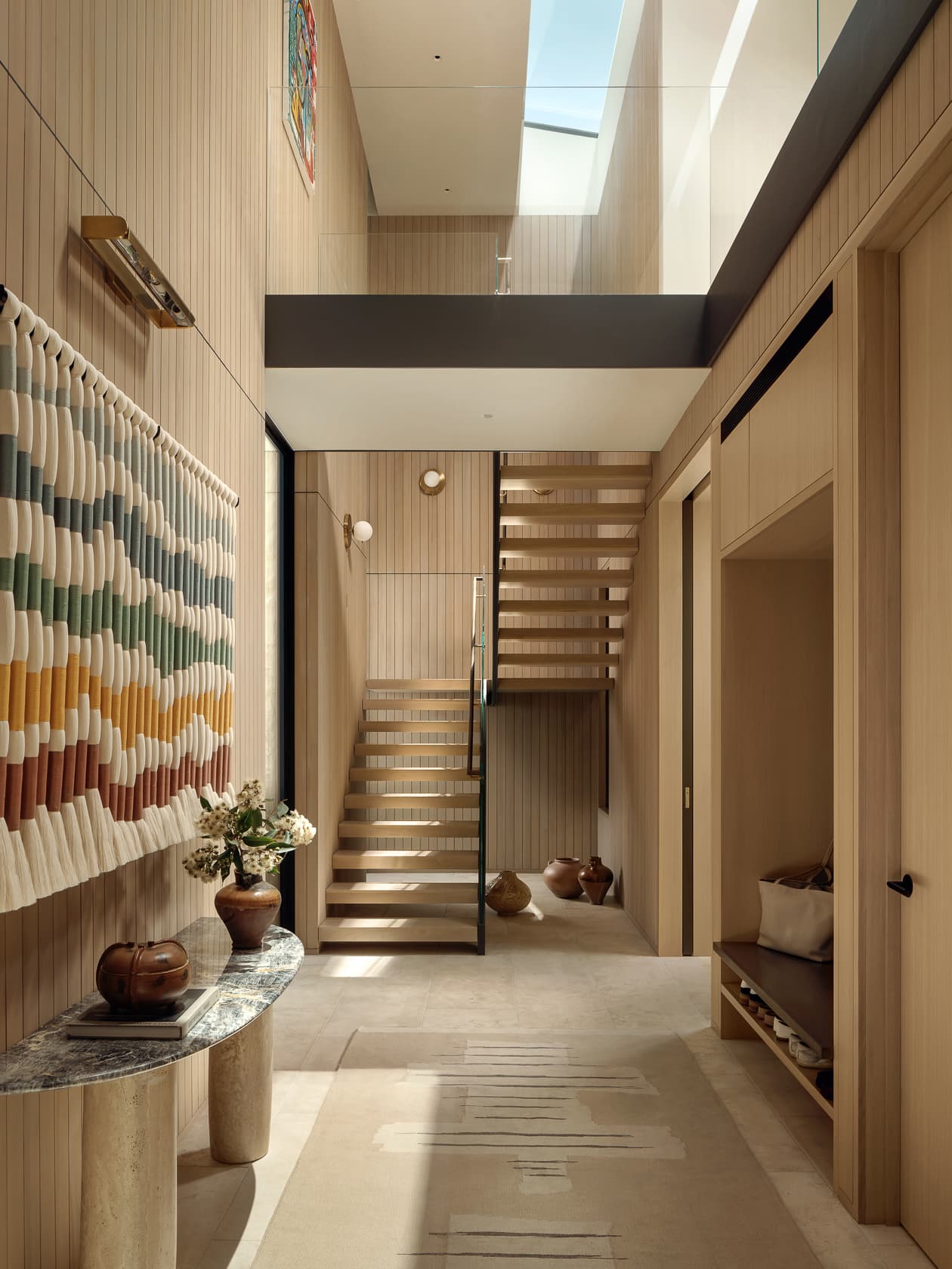A sunlit, wood-paneled hallway with a staircase leading up to a skylight-lit second floor.