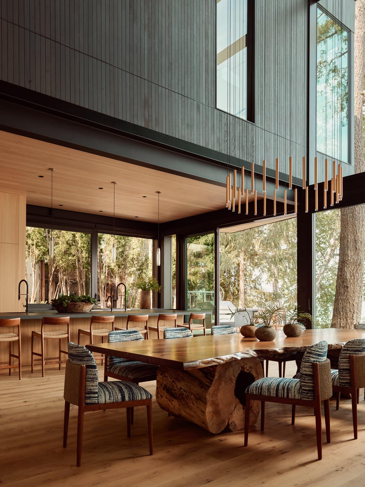 A spacious, modern dining room featuring a large wooden table and expansive forest views.