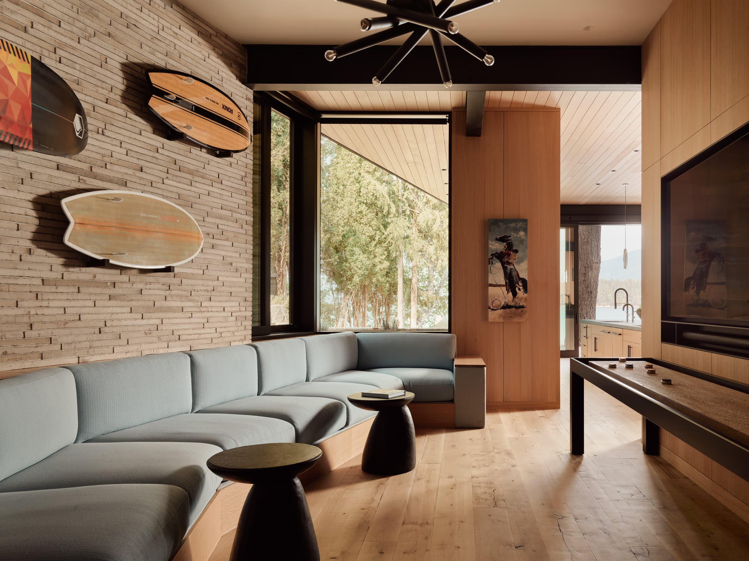 A modern living room with a blue sectional, surfboards on a brick wall, and a shuffleboard table.