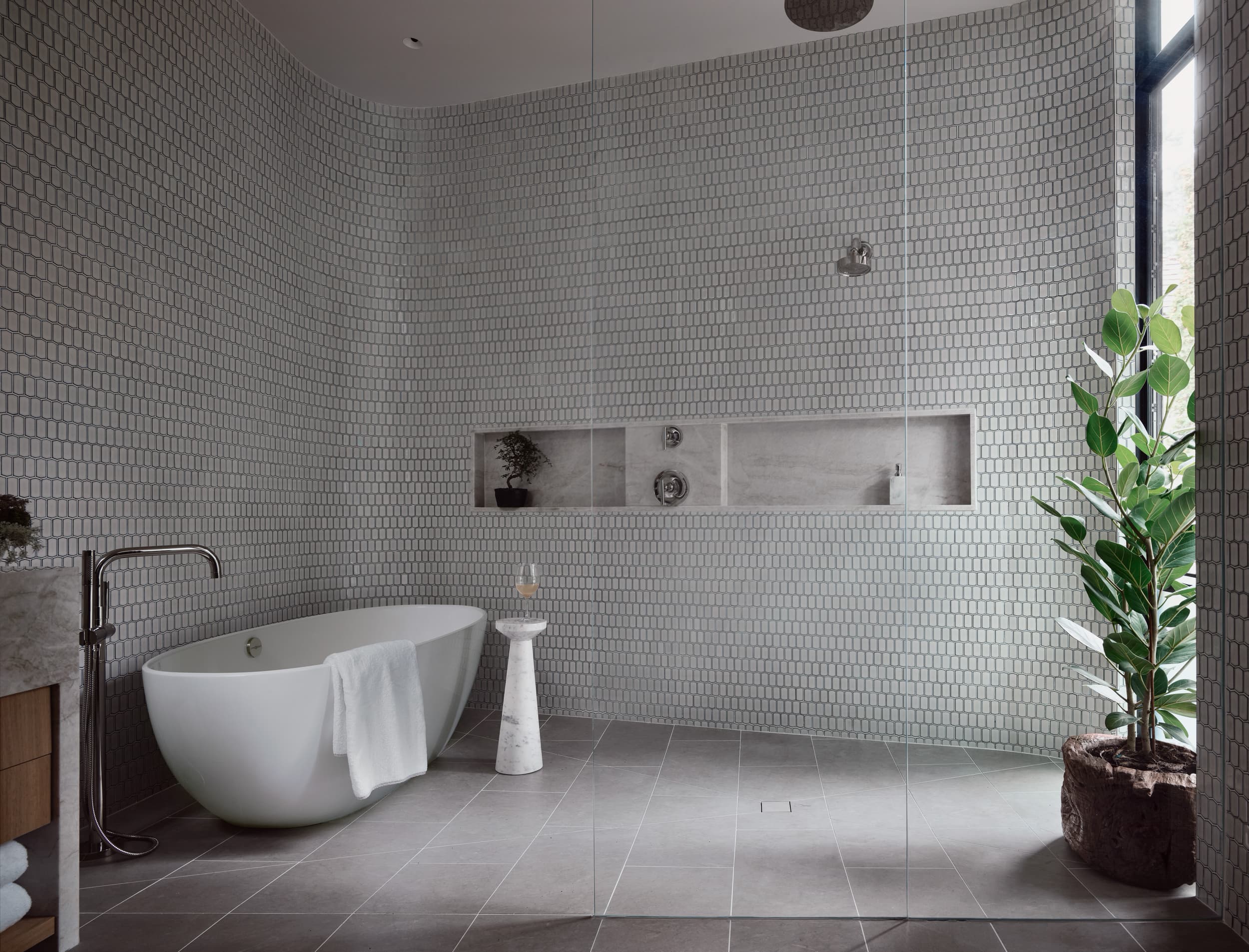 A modern bathroom with a white freestanding tub, a walk-in shower, and gray hexagonal wall tiles.