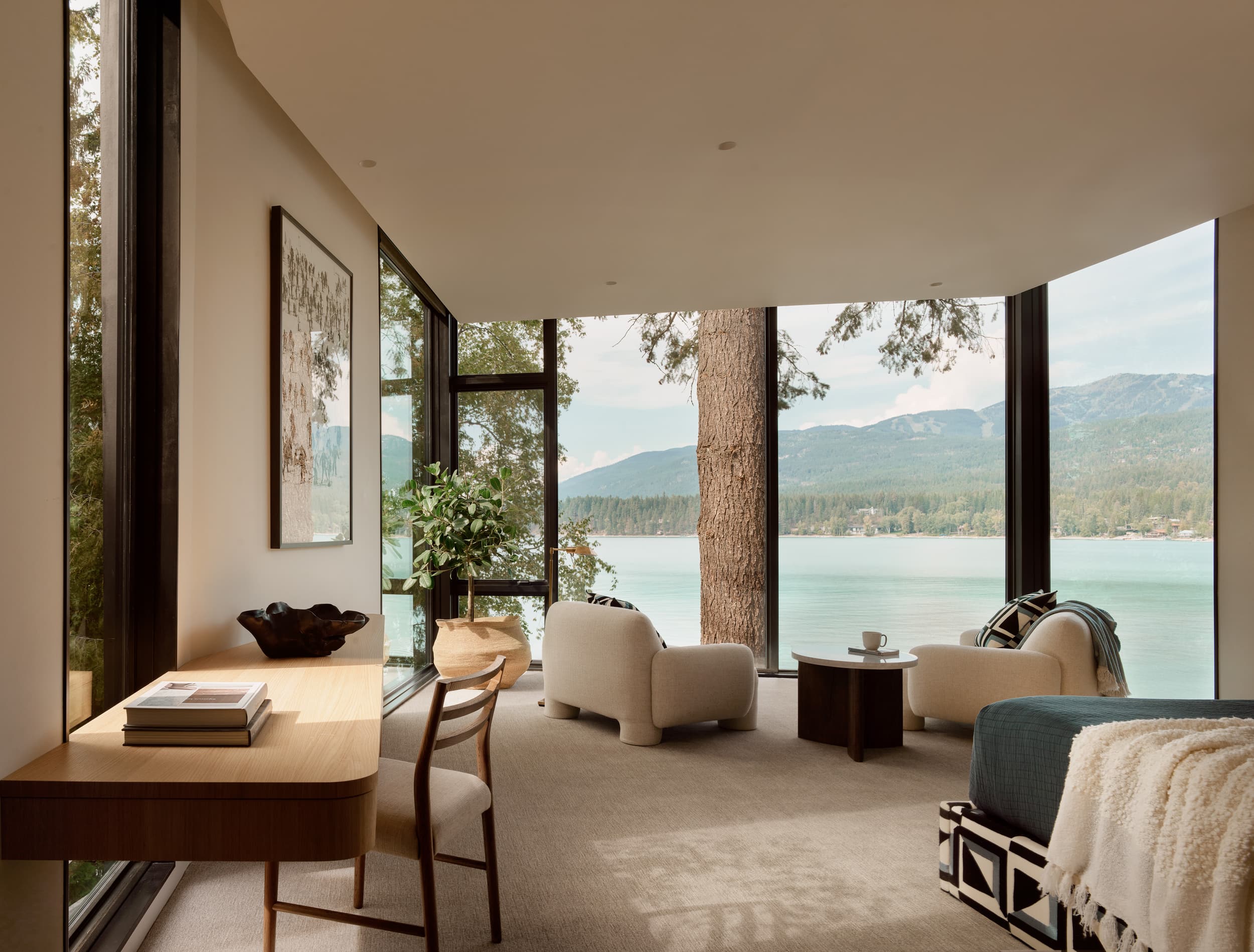 A serene bedroom with a curved wall of windows overlooking a tranquil lake and forest.