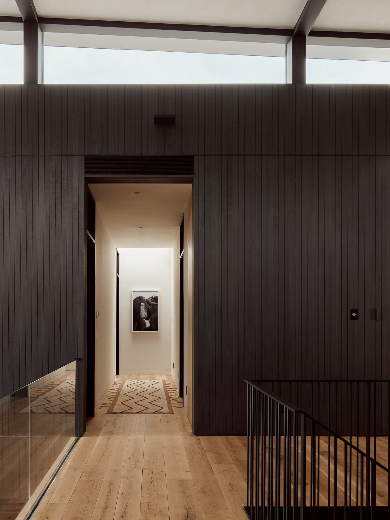 A modern landing with dark wood-paneled walls and a view into a brightly lit hallway.