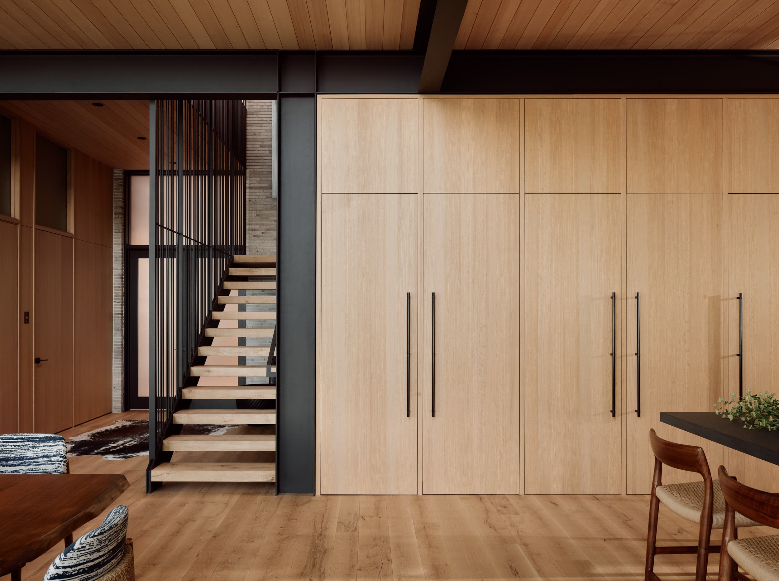 A modern home interior with light wood cabinetry and a black-framed staircase.
