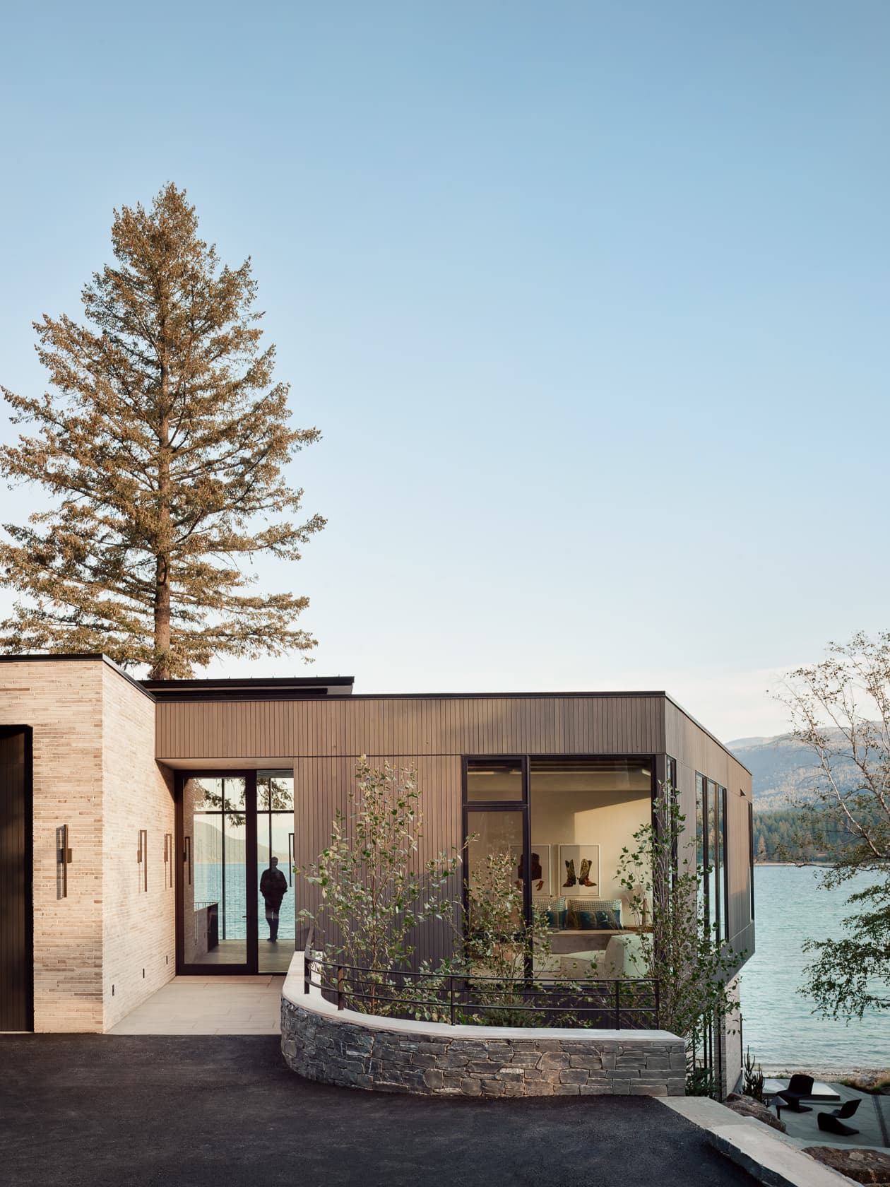 A modern house with wood siding and large windows overlooks a serene lake at dusk.