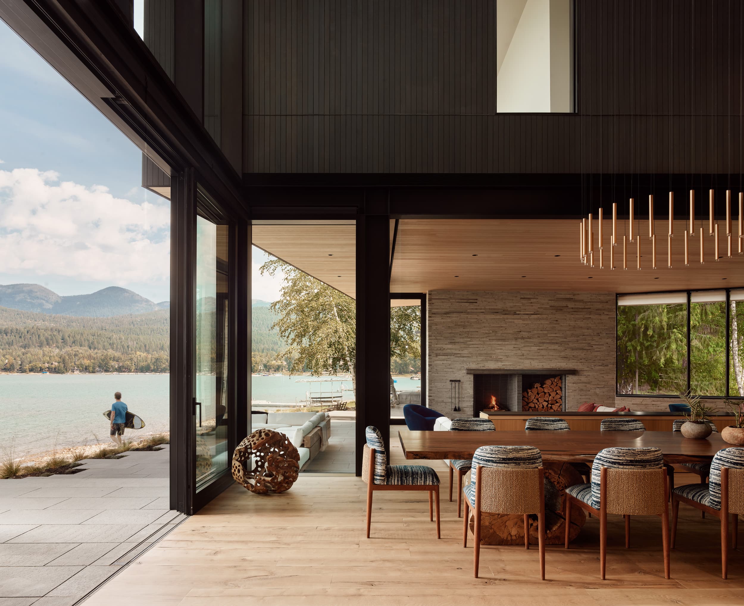 A modern dining room with glass walls opening onto a patio overlooking a calm lake.