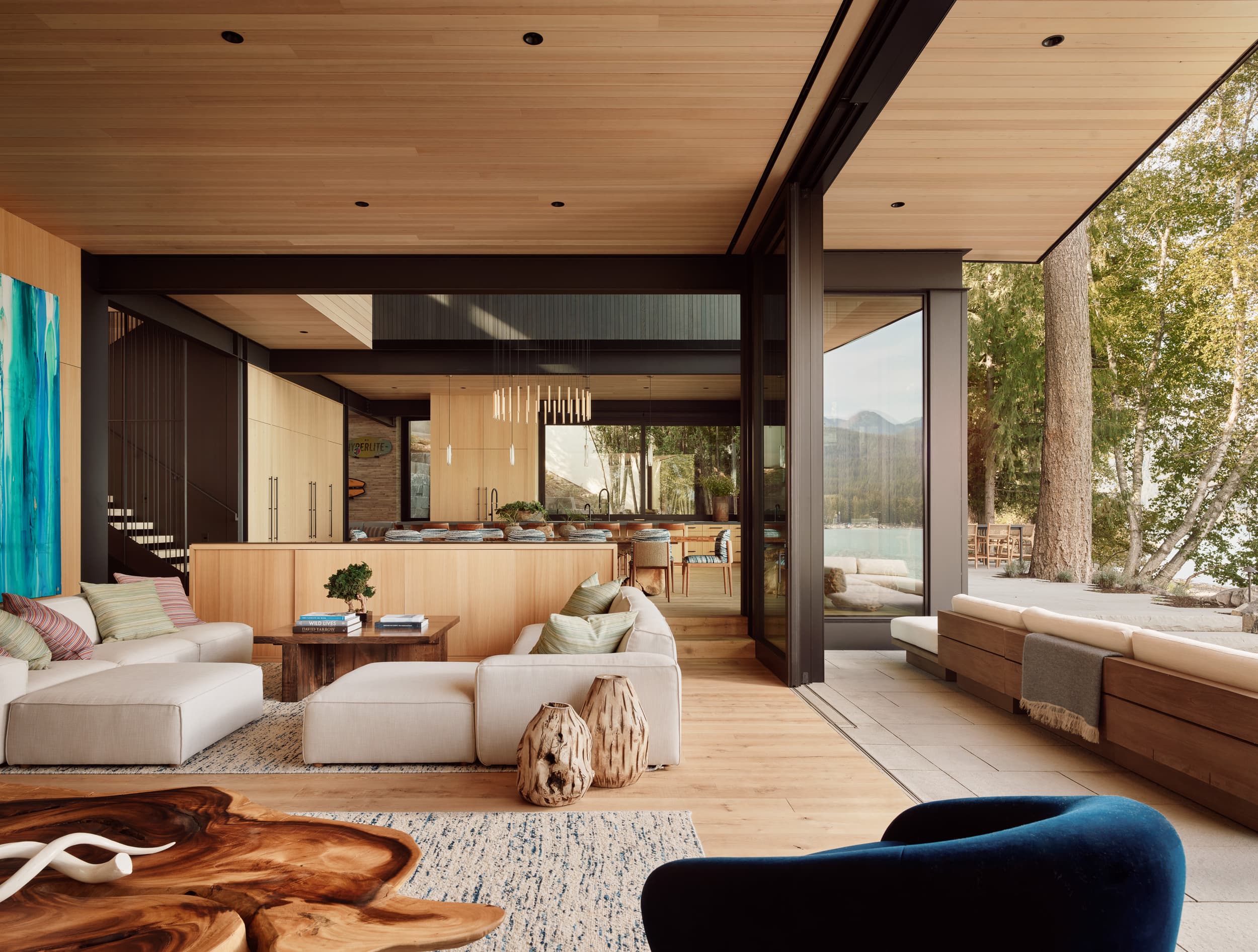 A modern living room with wood paneling opens via glass doors to a lakeside patio.