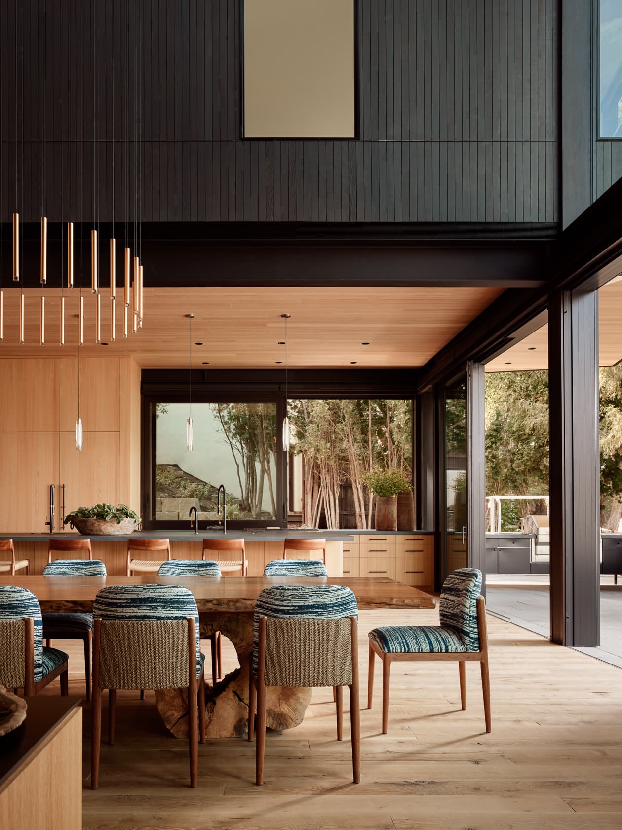 A spacious, modern dining room with wood paneling and large glass doors open to the outdoors.