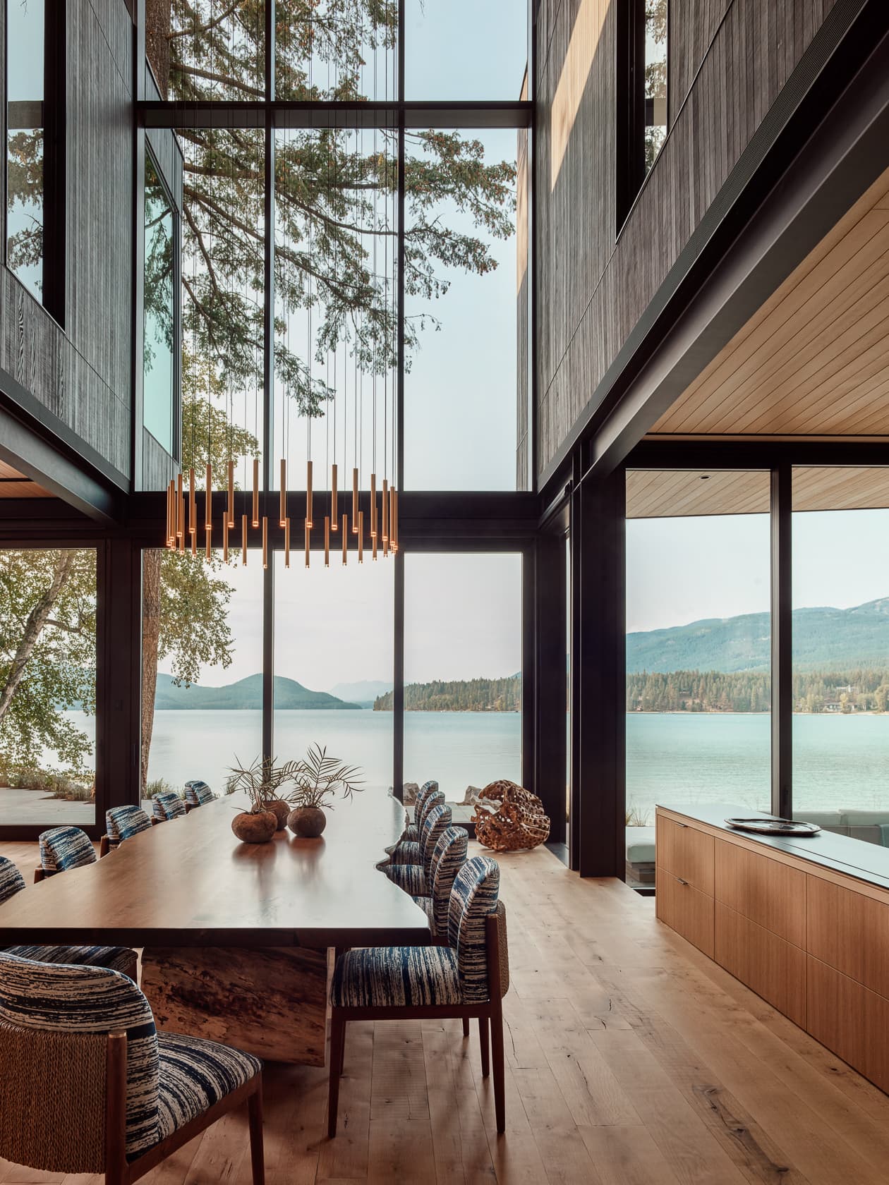 A modern dining room with floor-to-ceiling windows offering a panoramic view of a tranquil lake.