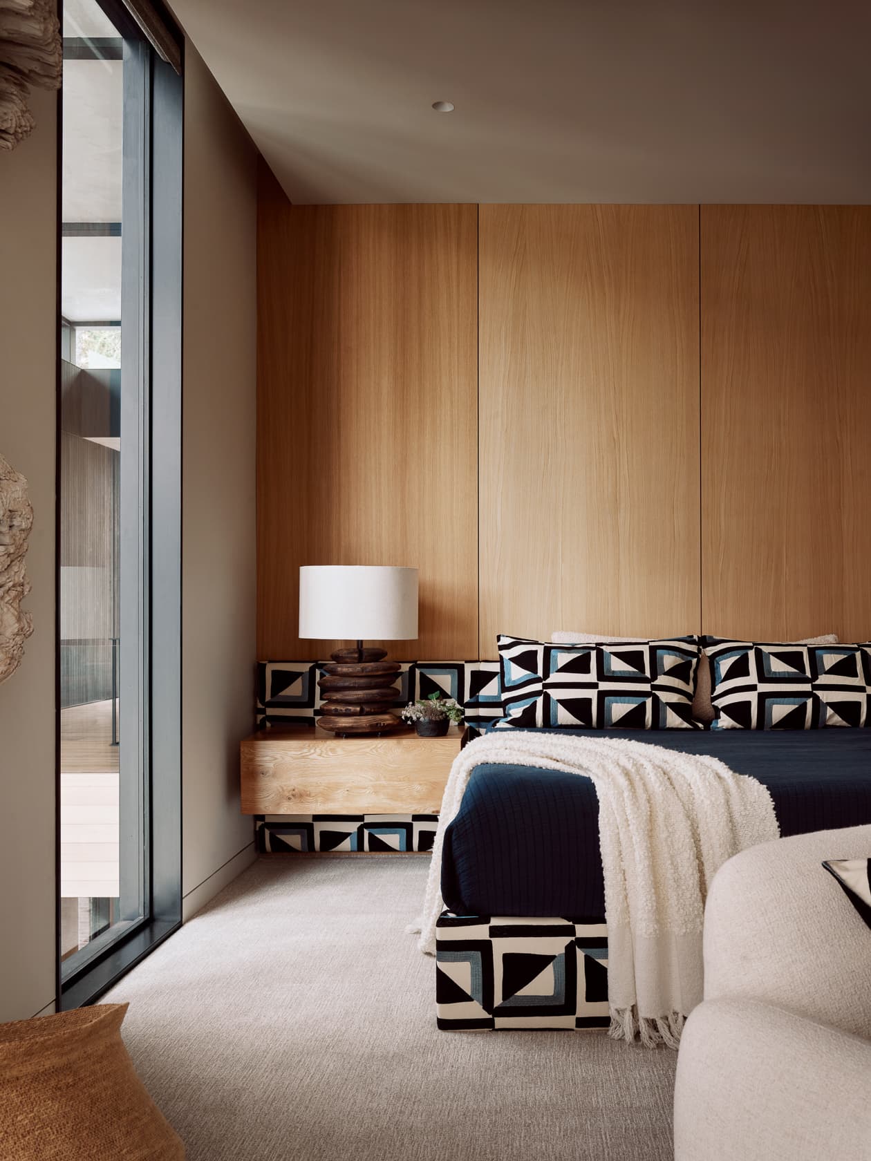 A modern bedroom with a light wood accent wall and a bed with a bold, geometric pattern.